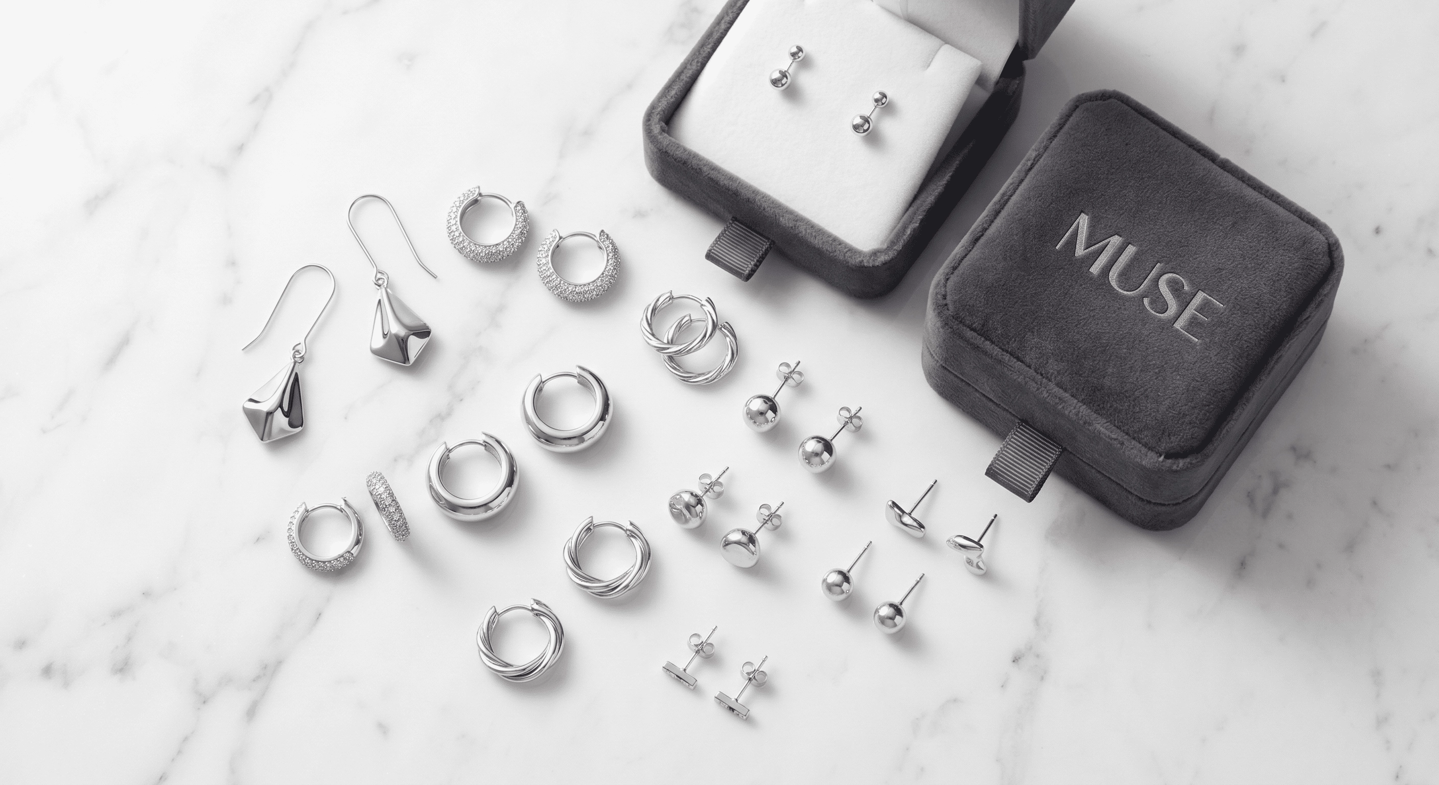 A diverse collection of modern silver drop earrings, huggies, and studs are arranged beautifully on a pristine white marble background (1) - Zhefan Jewelry