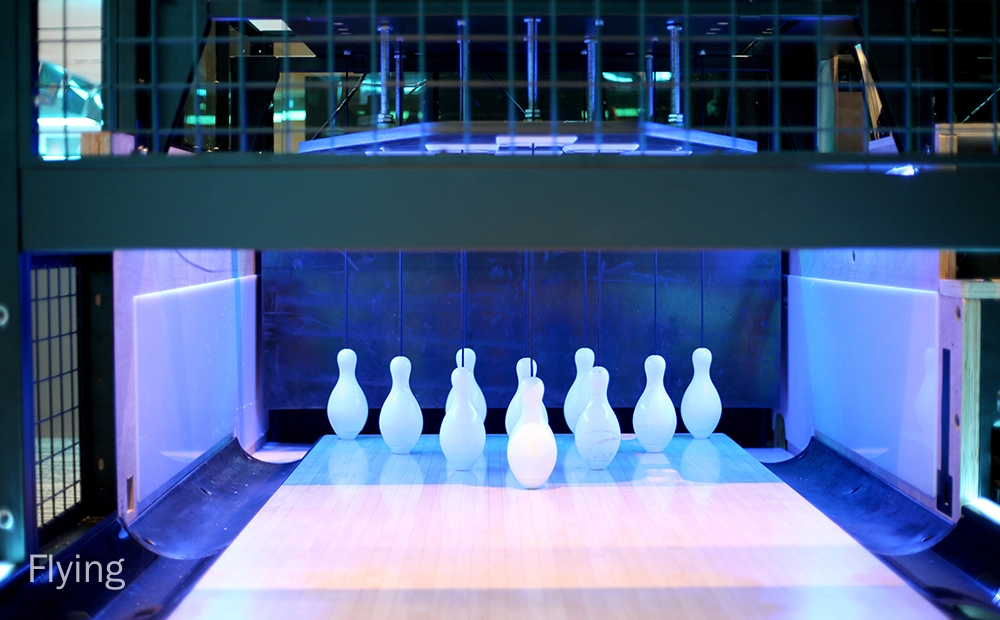 Flying - A bowling alley with the pins set up and ready to be bowled at. The pins are illuminated by a blue light.