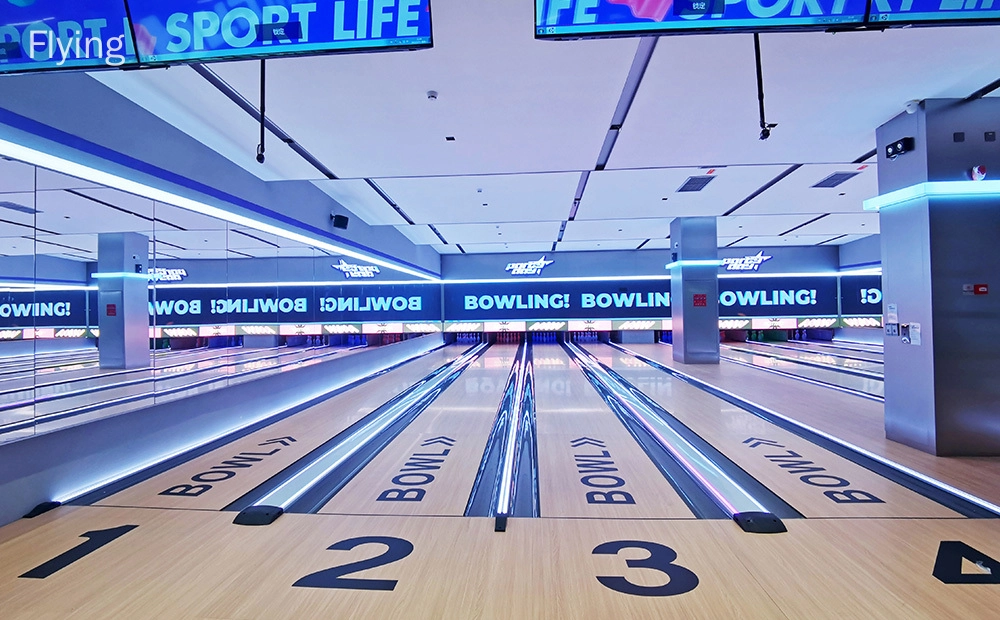 Flying - An image of a bowling alley with four lanes. The lanes are made of wood and have a shiny, waxed surface. The pins are set up at the end of each lane. There is a large screen at the end of the alley that shows the scores of the bowlers.