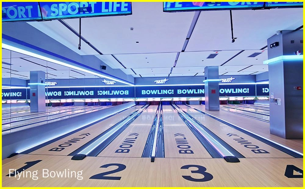 Flying Bowling - Imagem de uma pista de boliche com quatro pistas. As pistas são feitas de madeira e têm uma superfície brilhante e encerada. Os pinos são colocados no final de cada pista. Há uma tela grande no final da pista que mostra a pontuação dos jogadores.