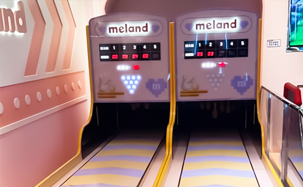 Two bowling lanes with pink and white walls and yellow and white floors.