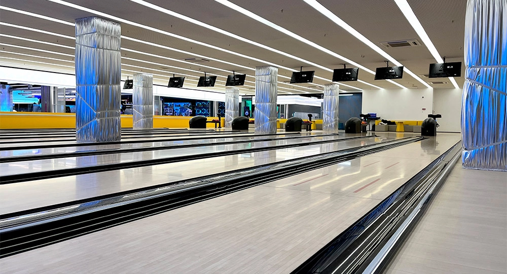 Flying - A modern bowling alley with multiple lanes, decorative silver-wrapped pillars, and overhead monitors.