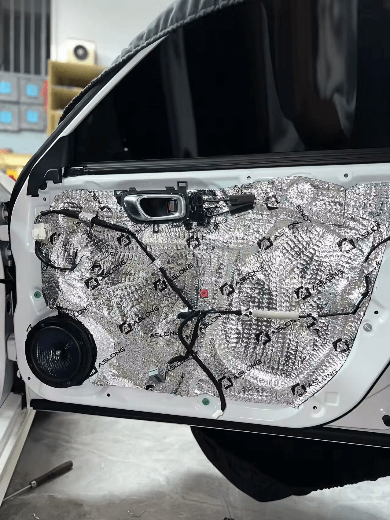 Car door with sound dampening material installed, exposing speaker and wiring. Car door with sound dampening material installed, exposing speaker and wiring.