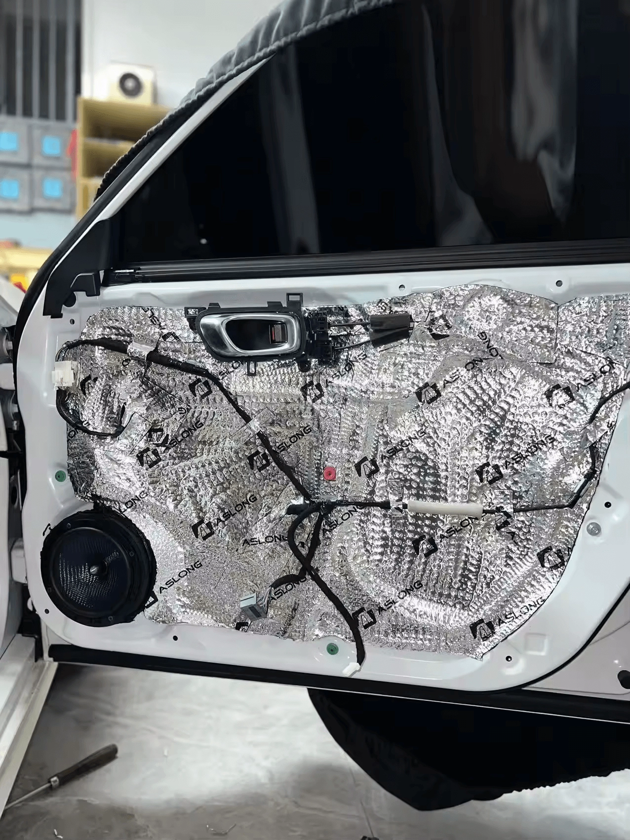 Car door with sound dampening material installed, exposing speaker and wiring.