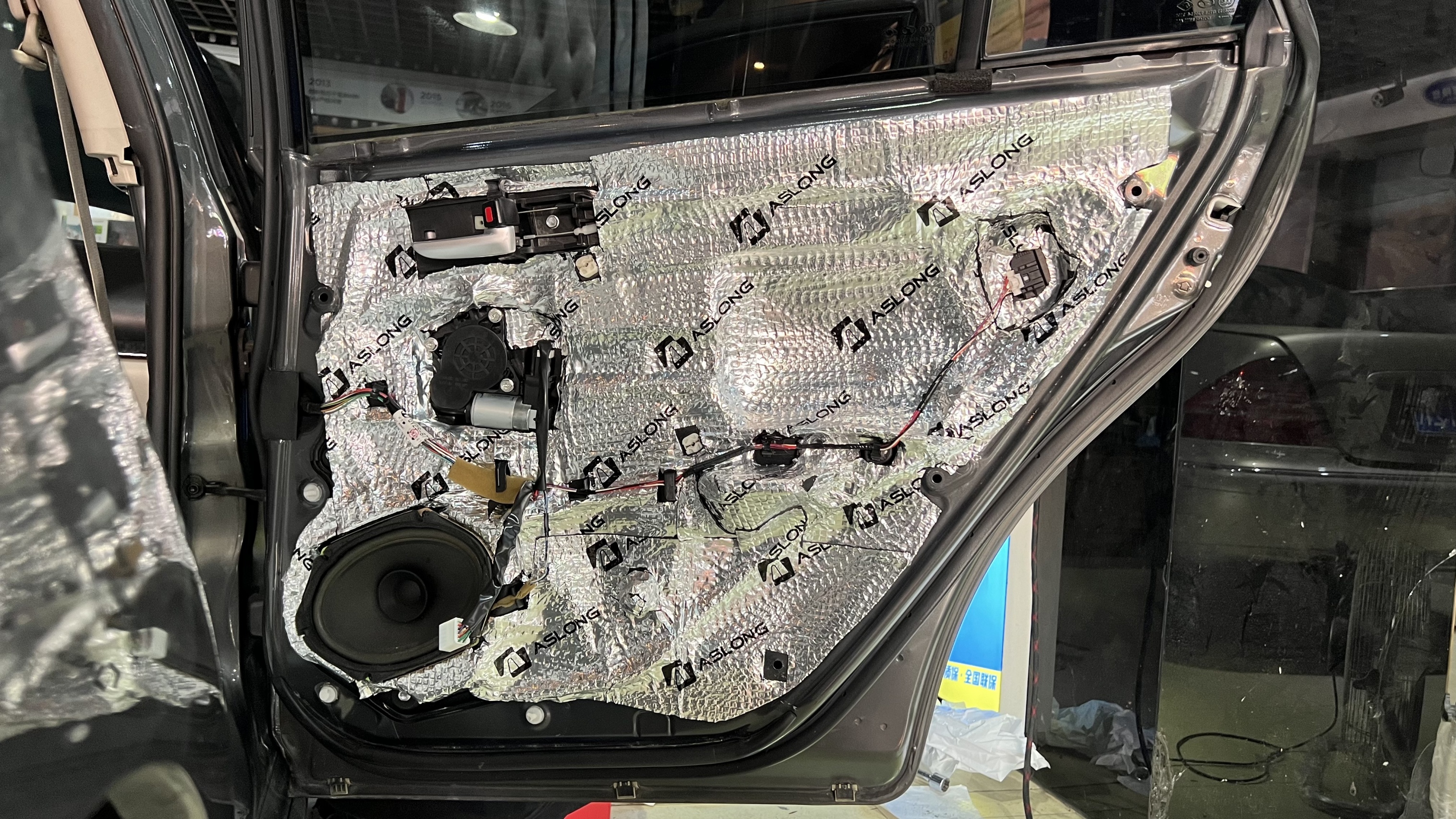 Car door panel with sound dampening insulation installed, showing speaker and wiring.