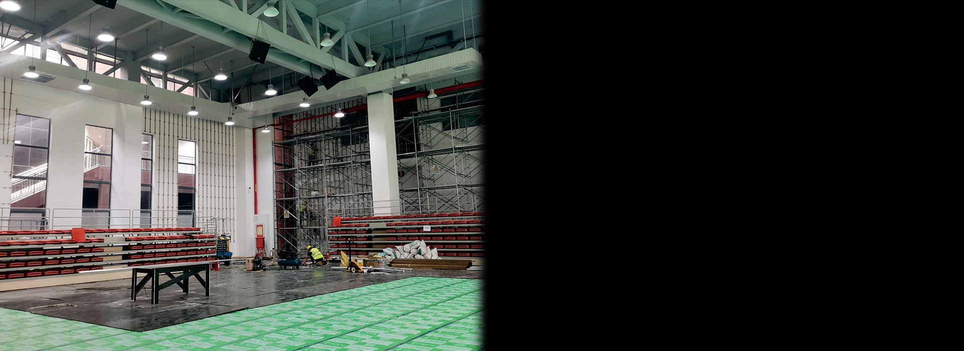 Indoor arena under construction, showing seating, scaffolding, and workers.