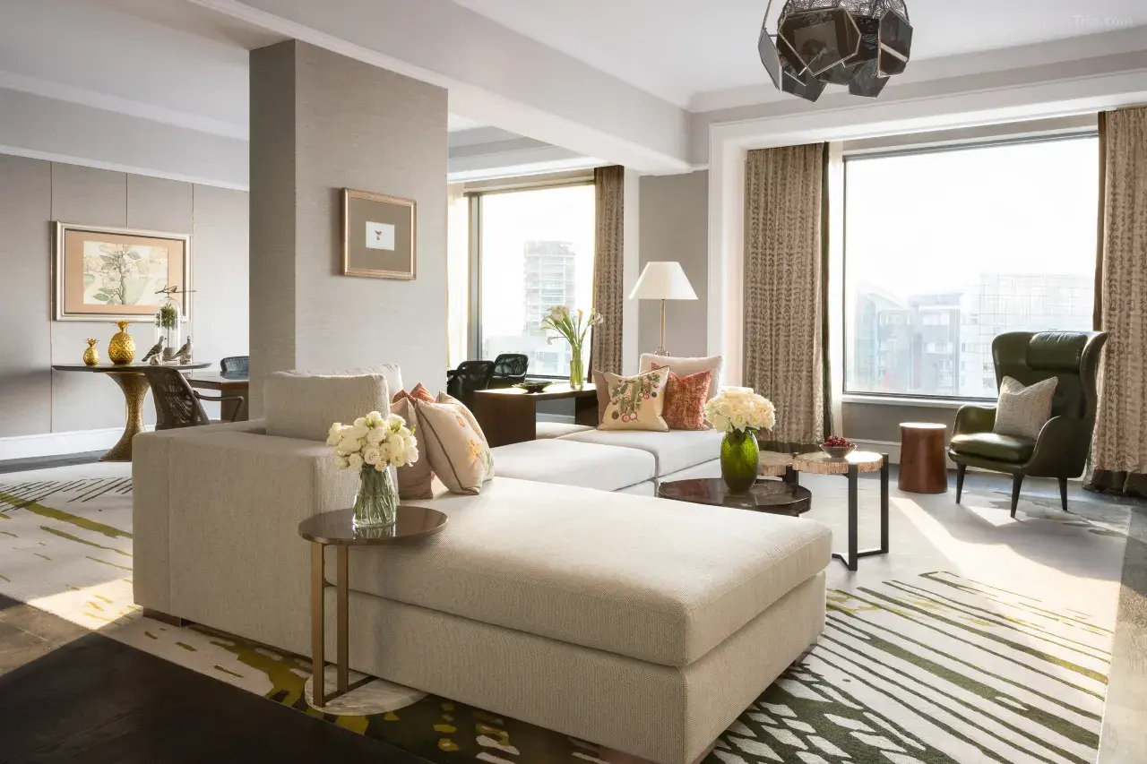 Modern luxury hotel suite with a beige sectional sofa and city views.