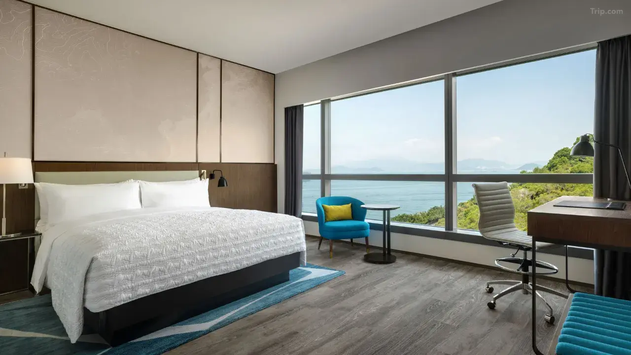 Modern hotel room with a large bed, desk, and floor-to-ceiling ocean views...