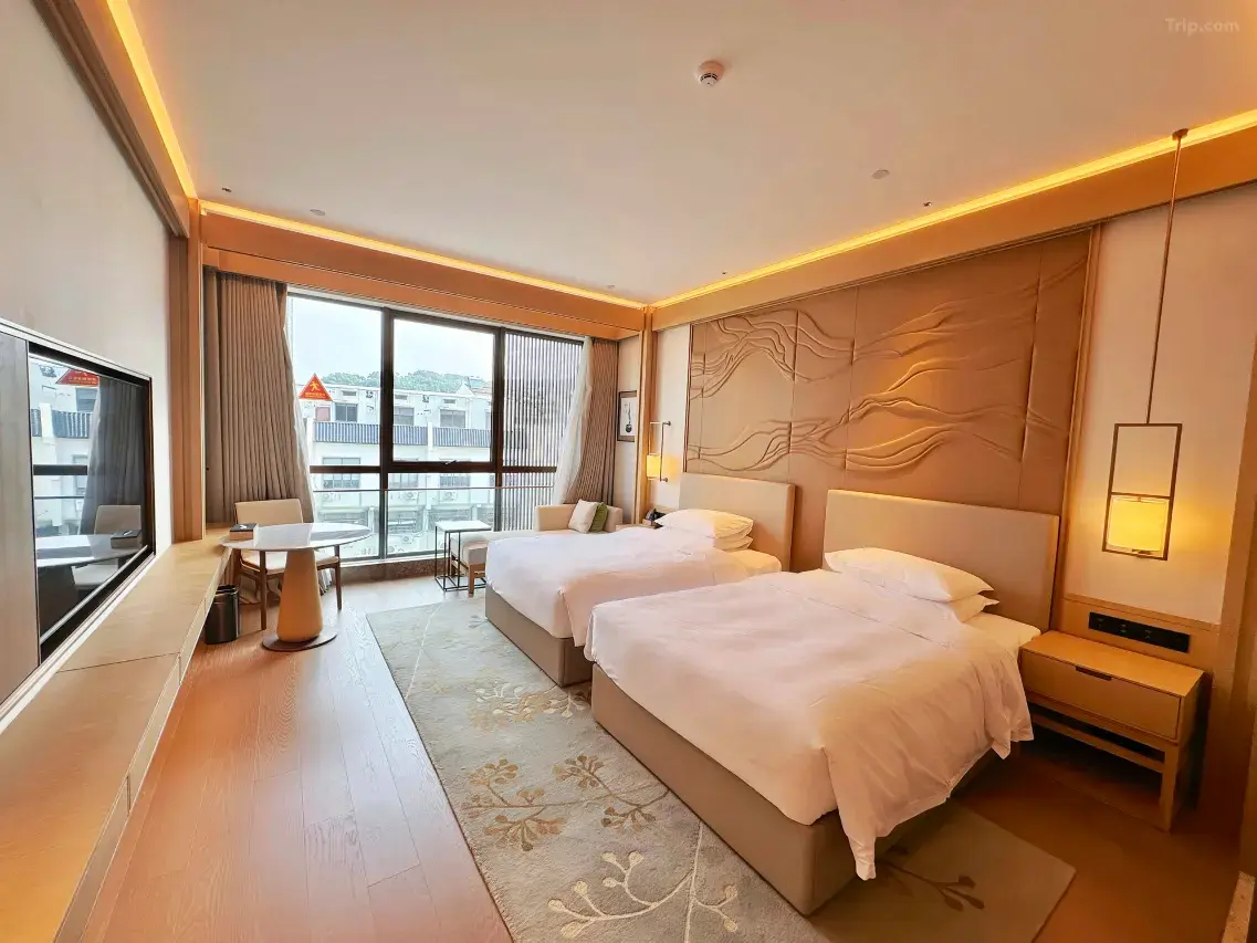 Modern hotel room with two twin beds, large window, and textured wall panel.