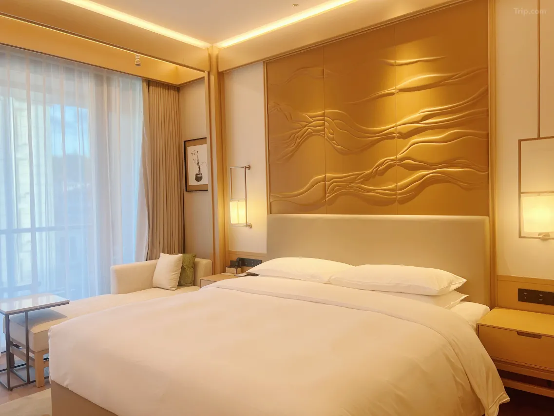 Modern hotel room with a large bed, warm lighting, and wavy wall art.