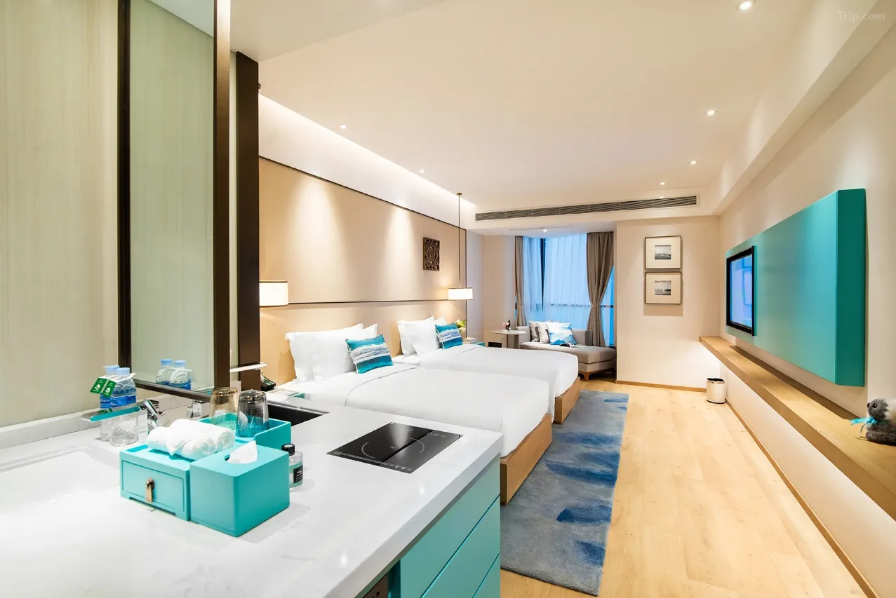 Modern hotel room with two beds, kitchenette, and window seating.