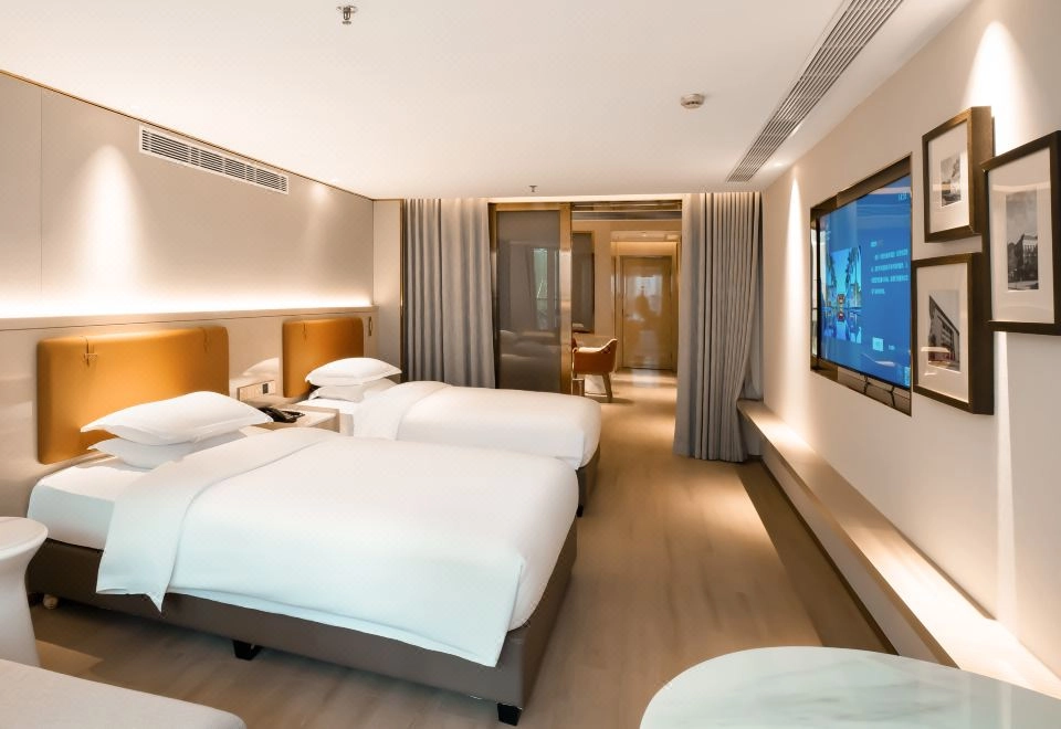 Modern hotel twin room with warm lighting, two beds, and wall-mounted TV.
