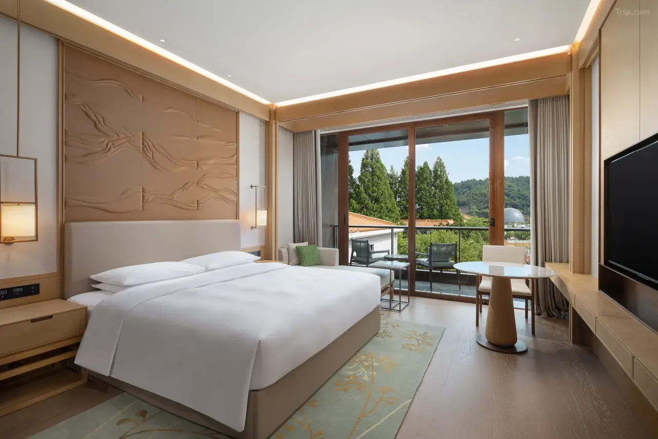 Modern luxury hotel room with a balcony overlooking trees.