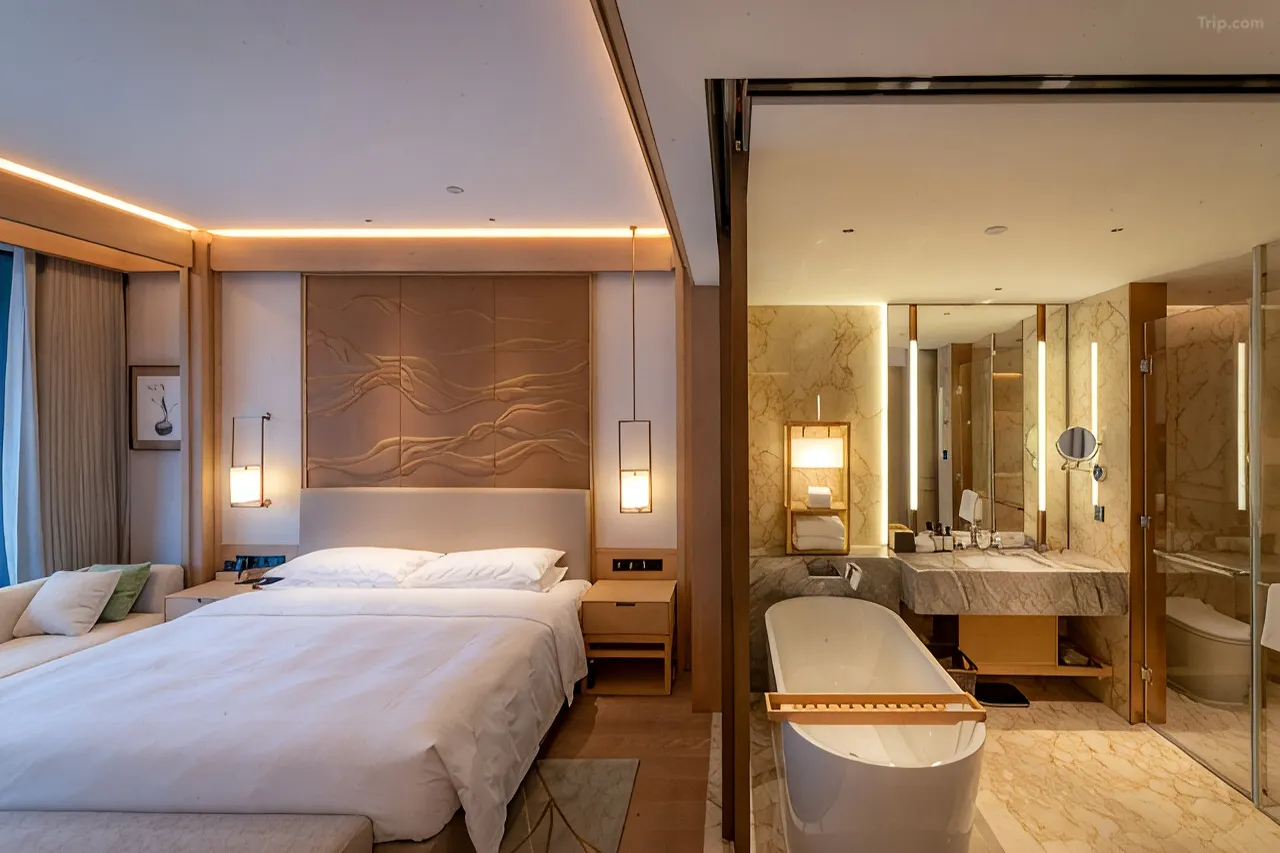 Modern luxury hotel suite with a large bed and marble bathroom.