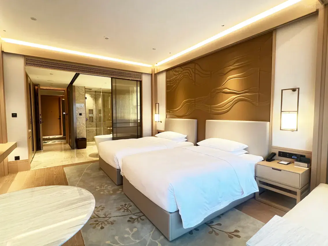 Modern hotel room with two twin beds and a golden textured headboard wall.