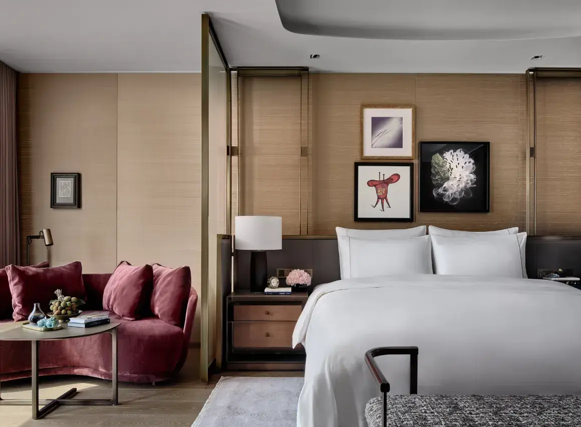 Modern luxury hotel suite with a white bed, velvet sofa, and neutral decor.