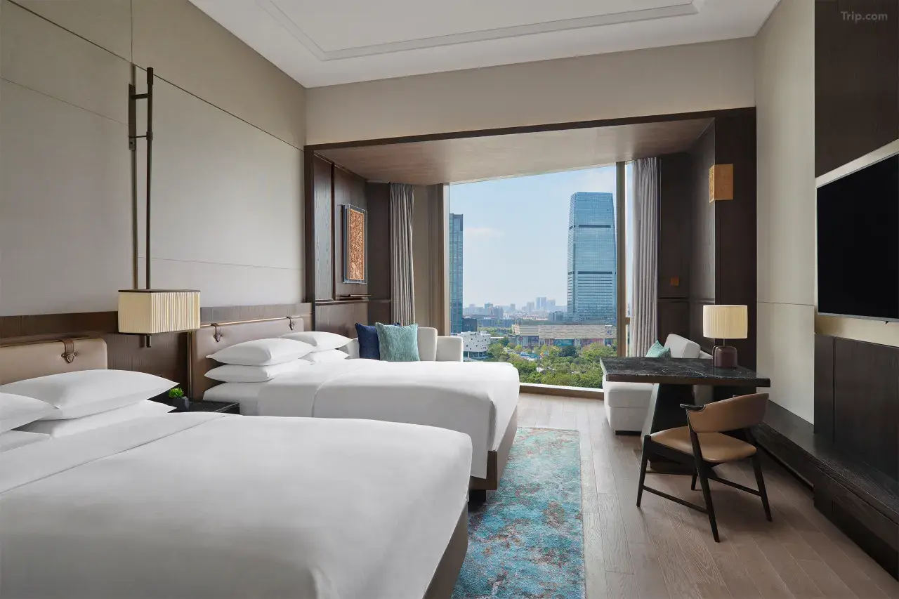 Modern hotel room with two twin beds and a large window overlooking a city.