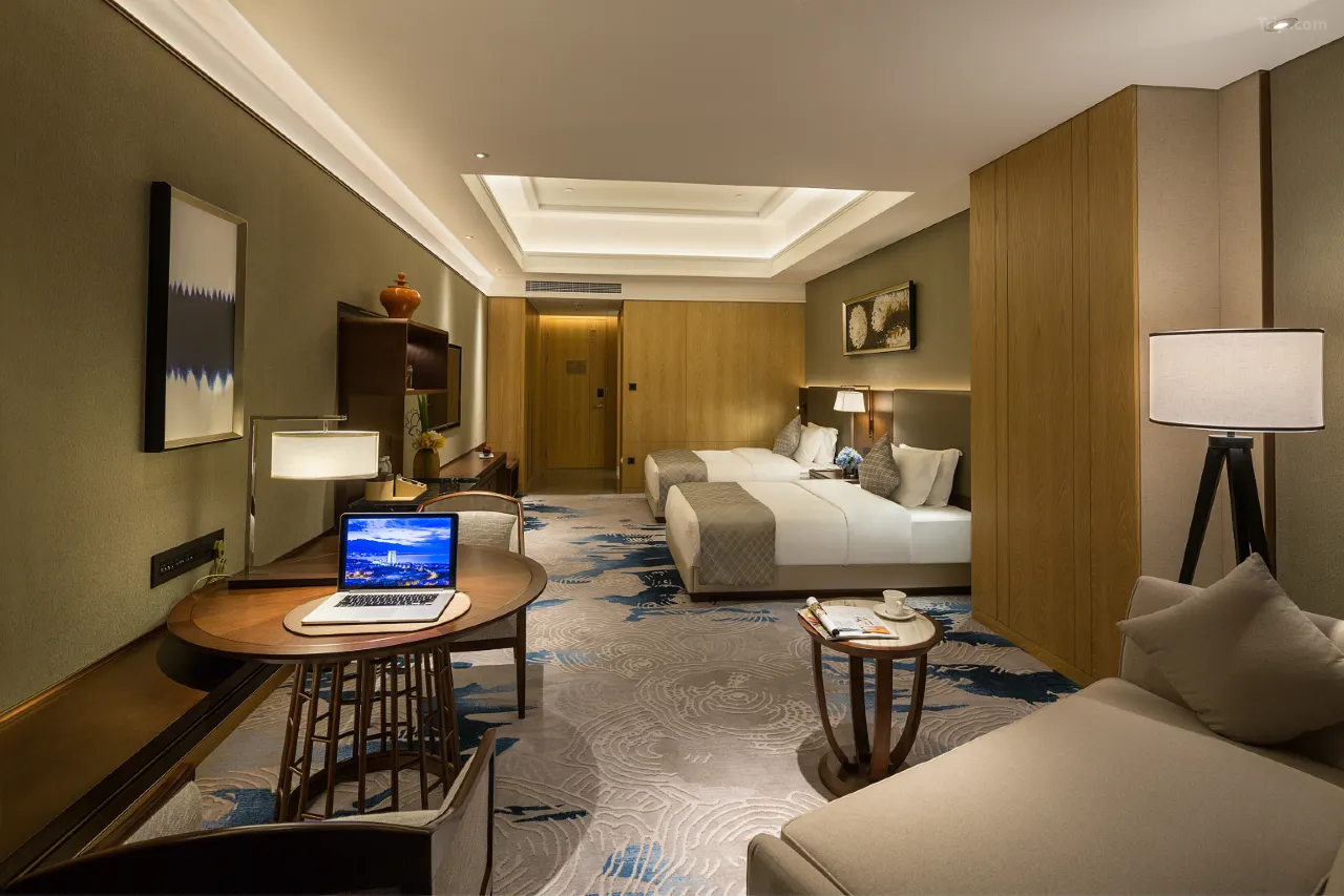 Modern hotel room with two twin beds, a desk, and a seating area.