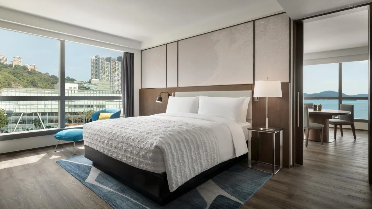 Modern hotel suite with a large bed, city views, and an adjacent dining area...