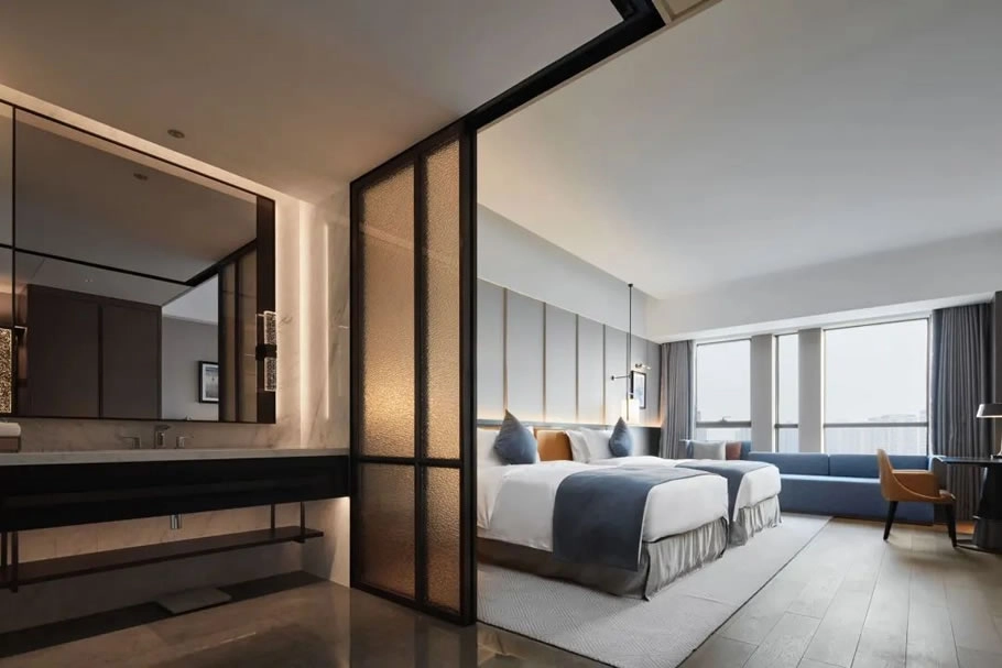 Hotel suite with two beds, a blue sofa, and a partial view of the bathroom.