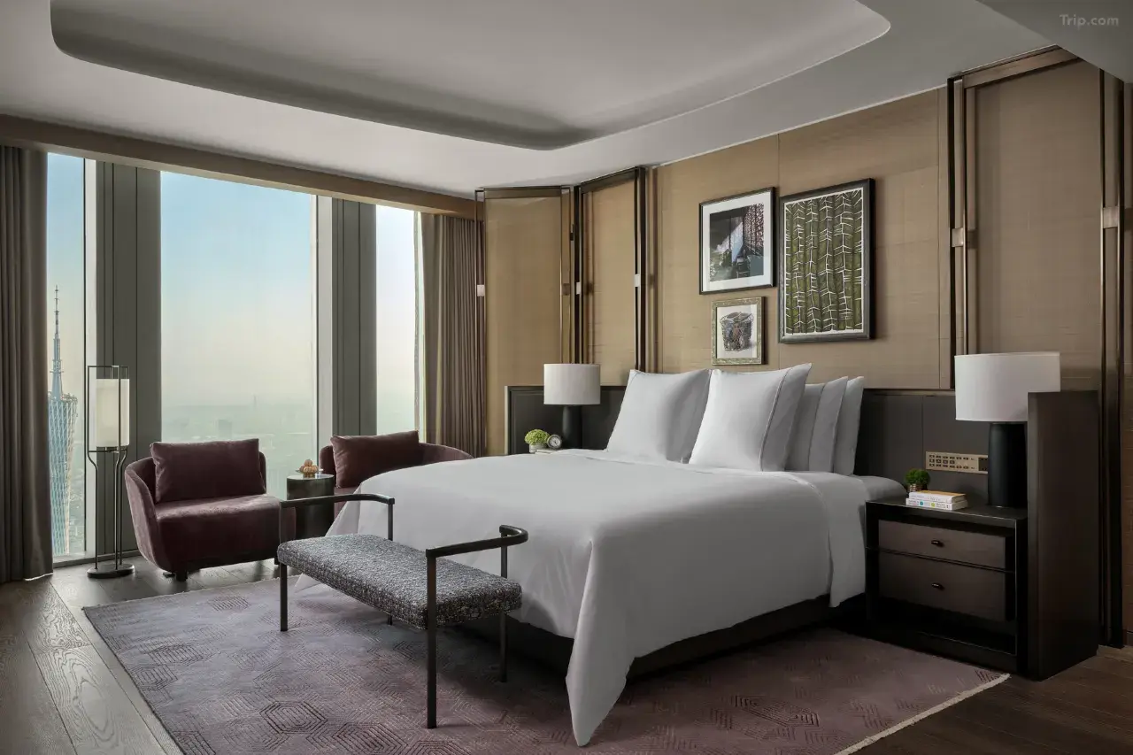 Modern luxury hotel room with a city view, king bed, and velvet armchairs.