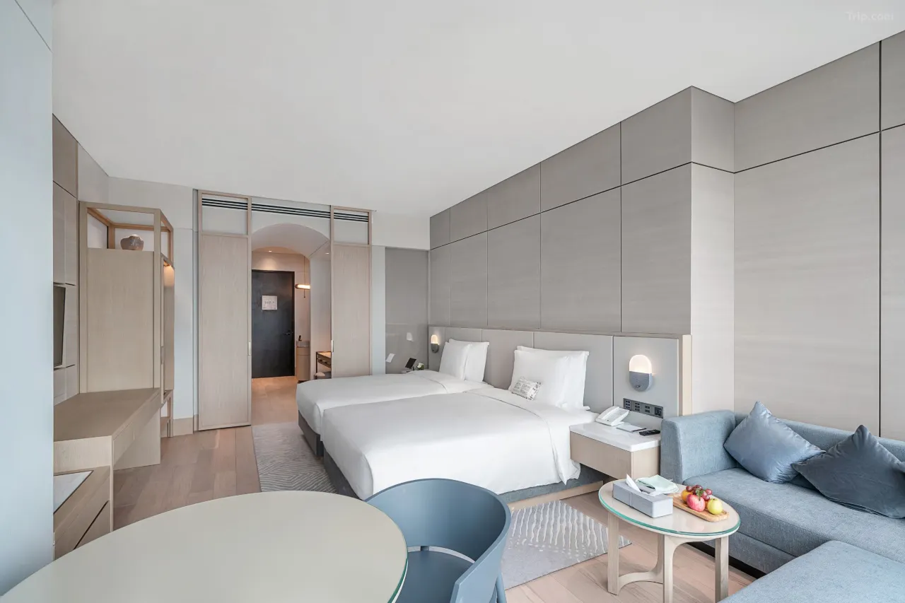 Modern hotel room with two twin beds, a blue sofa, and minimalist decor.