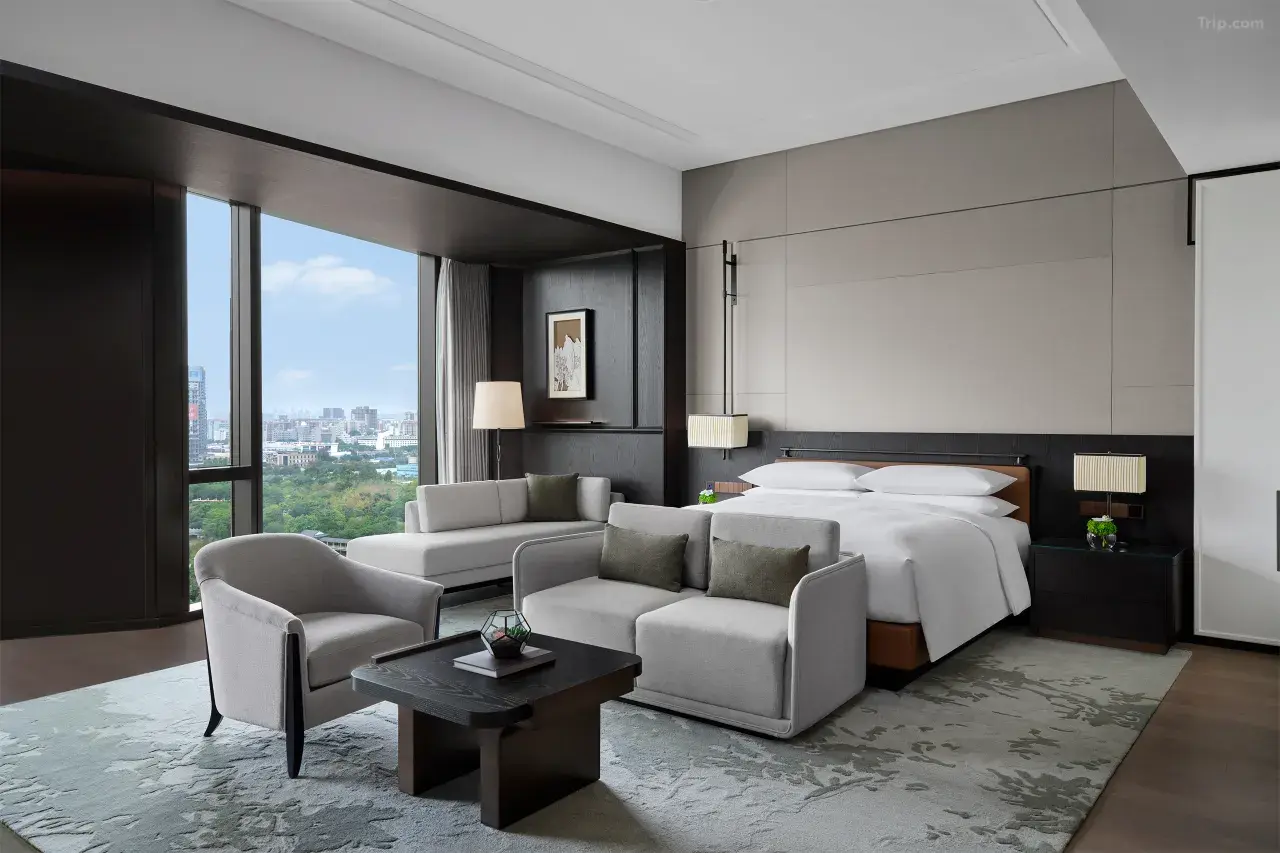 Modern luxury hotel suite with a city view, seating area, and king bed.