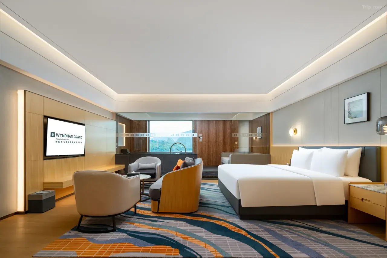 Modern hotel room with king bed, sofa, TV, and large window.