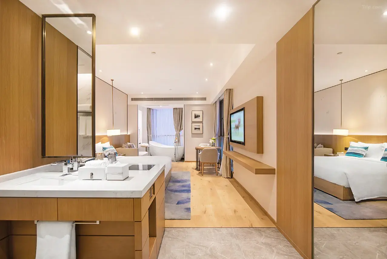 Modern hotel suite with a vanity, bedroom, living area, and bathtub by a window.