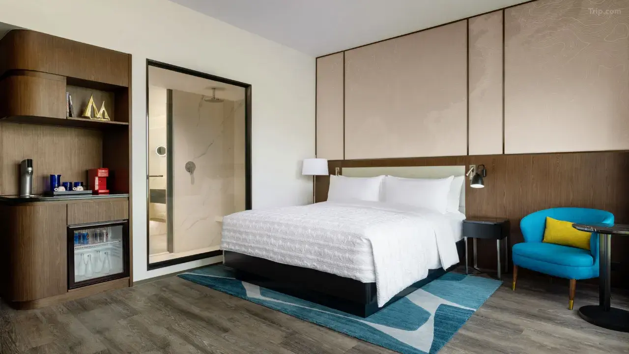Modern hotel room with white bed, blue armchair, and wood accents...