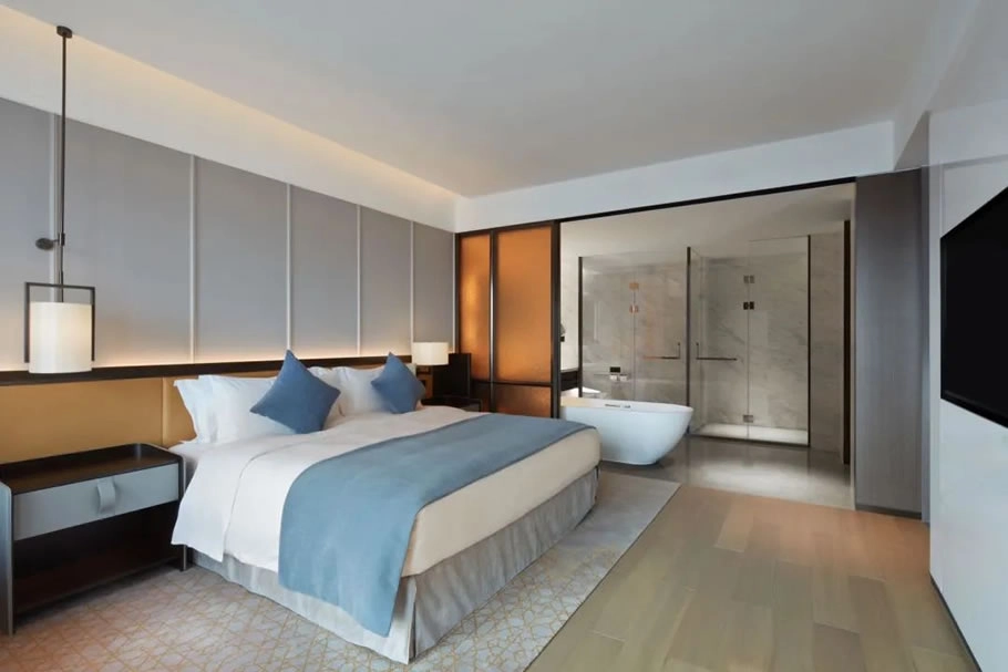 Hotel suite bedroom with king bed and adjacent bathroom featuring a modern tub and glass shower.