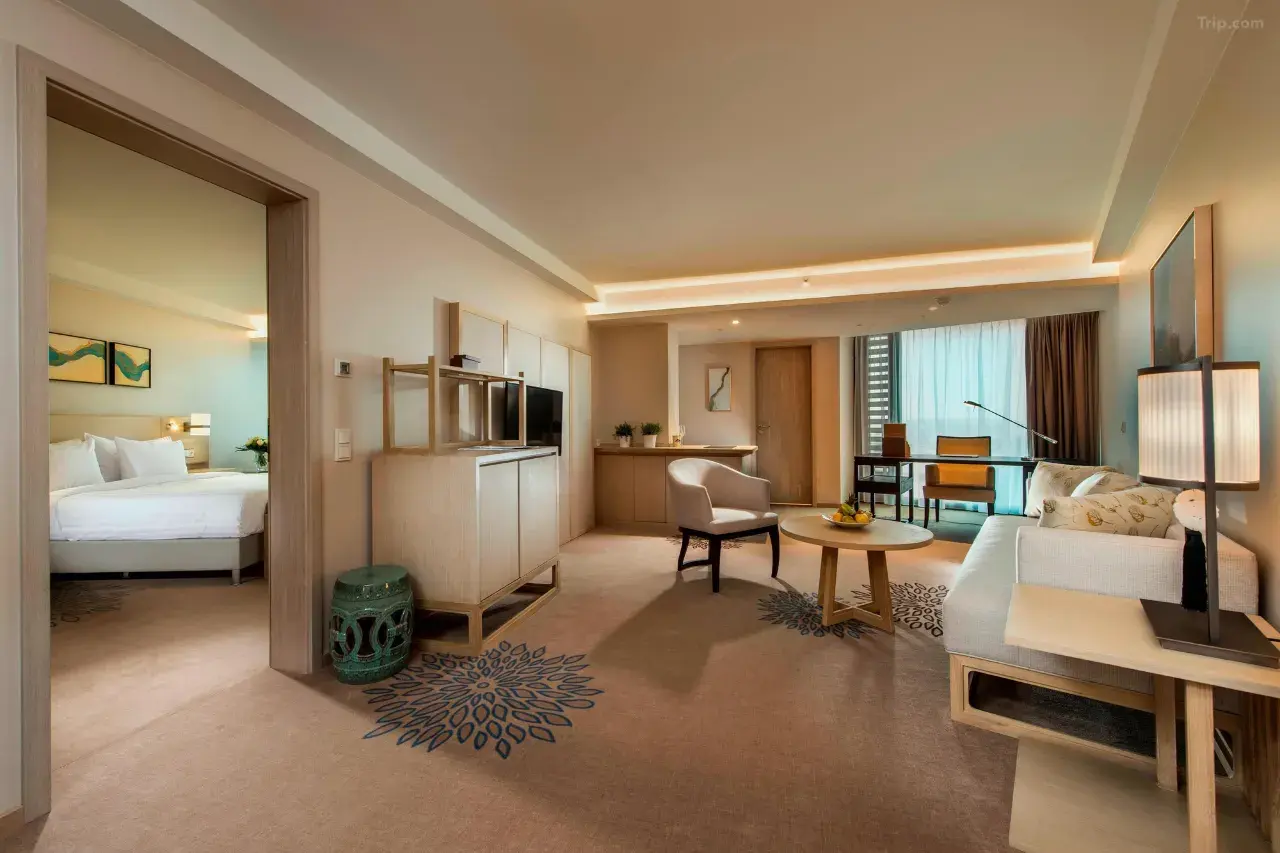 Modern hotel suite with a living area, workspace, and view into the bedroom.