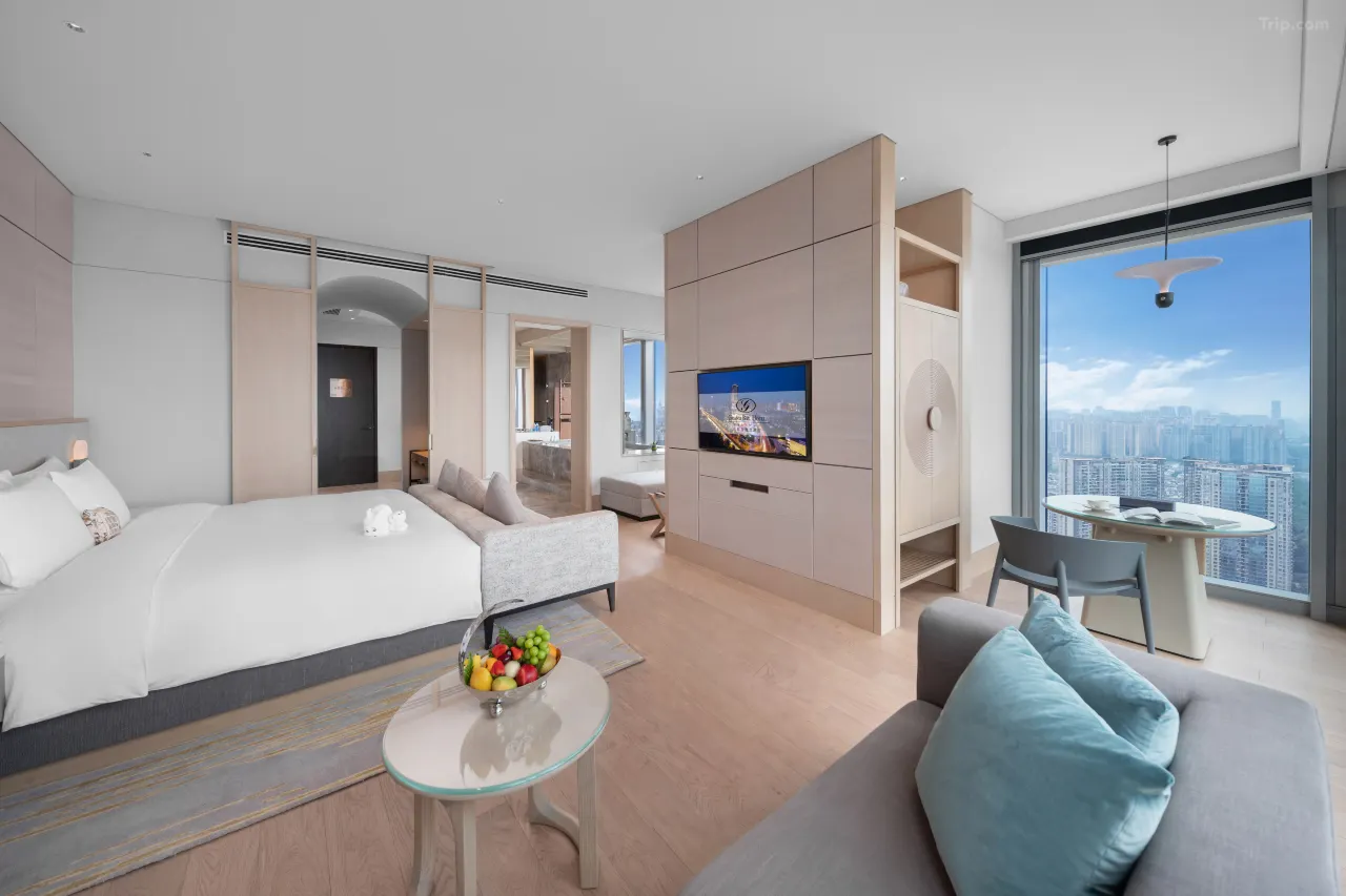 Modern luxury hotel suite with city views, white bed, and seating area.