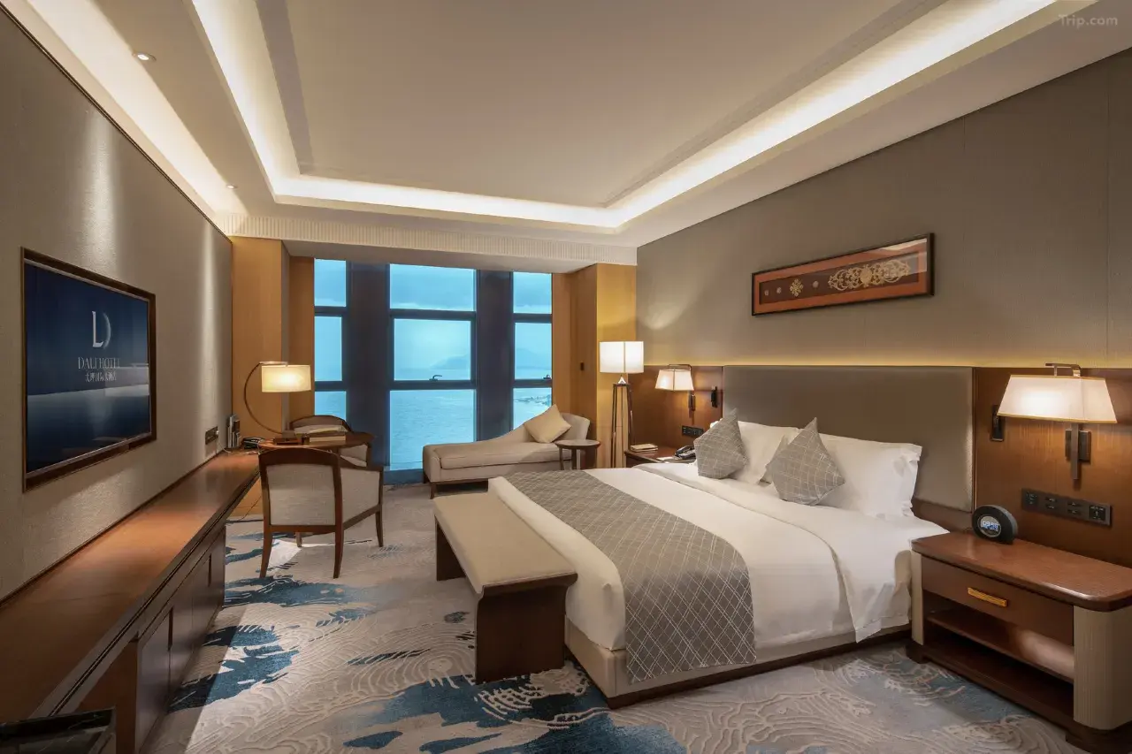 Modern luxury hotel room with a king bed and ocean view through large windows.