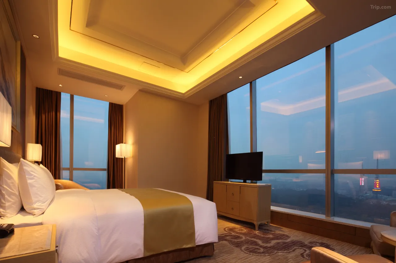 Luxurious hotel room with a large bed, golden accents, and a panoramic city view.