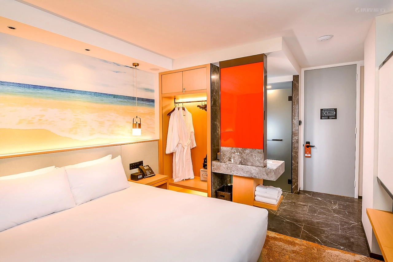 Modern hotel room with a large bed, beach mural, open closet, and bathroom entrance.