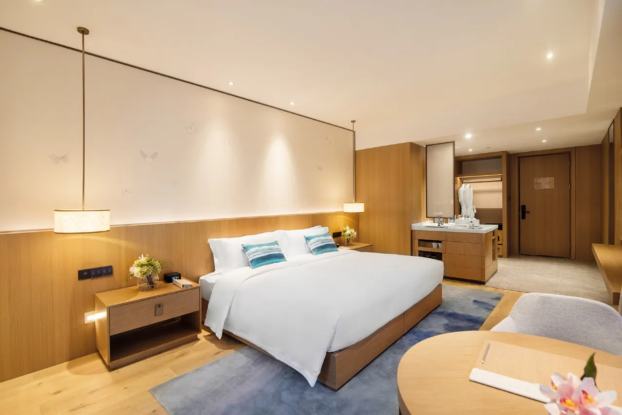 Modern hotel room with king bed, wood accents, and vanity area.