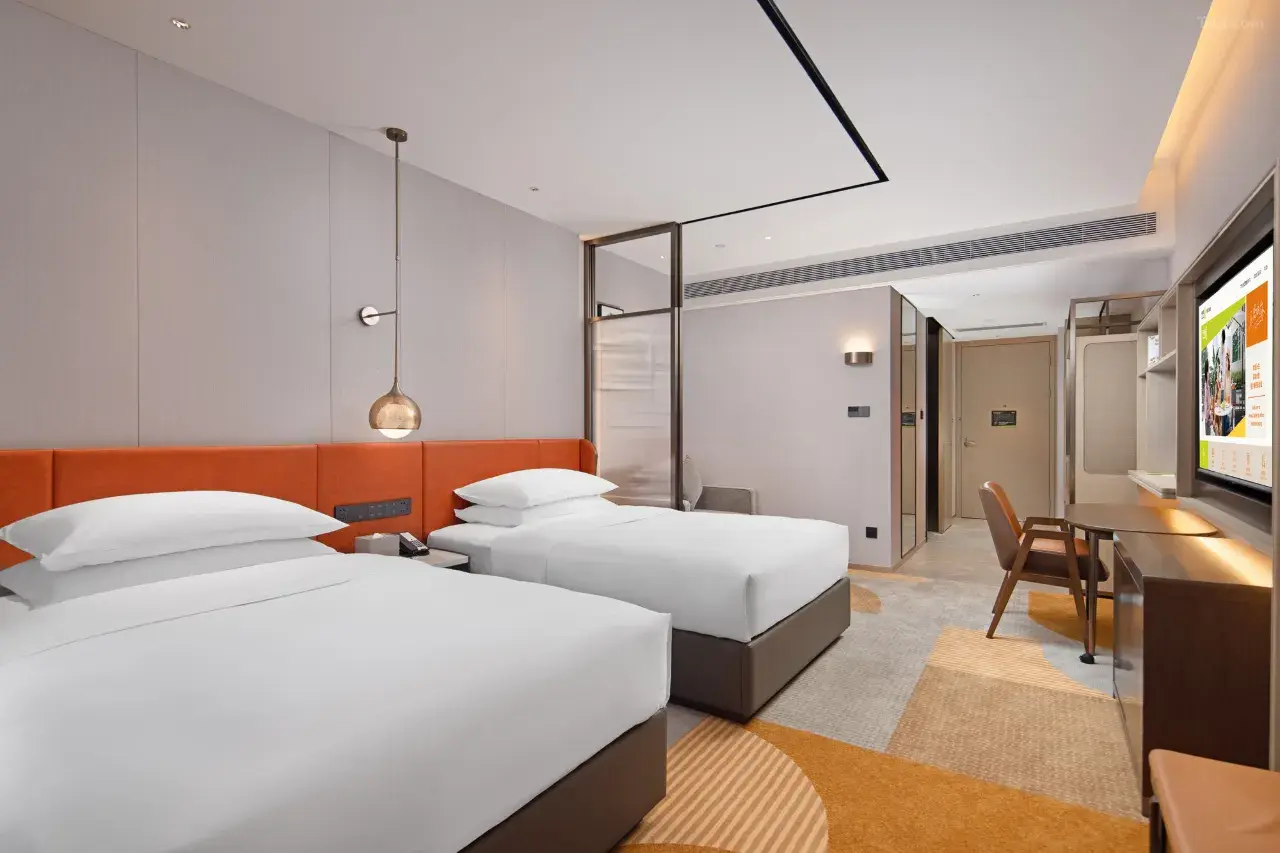 Modern hotel room with two twin beds, orange headboard, and work desk.