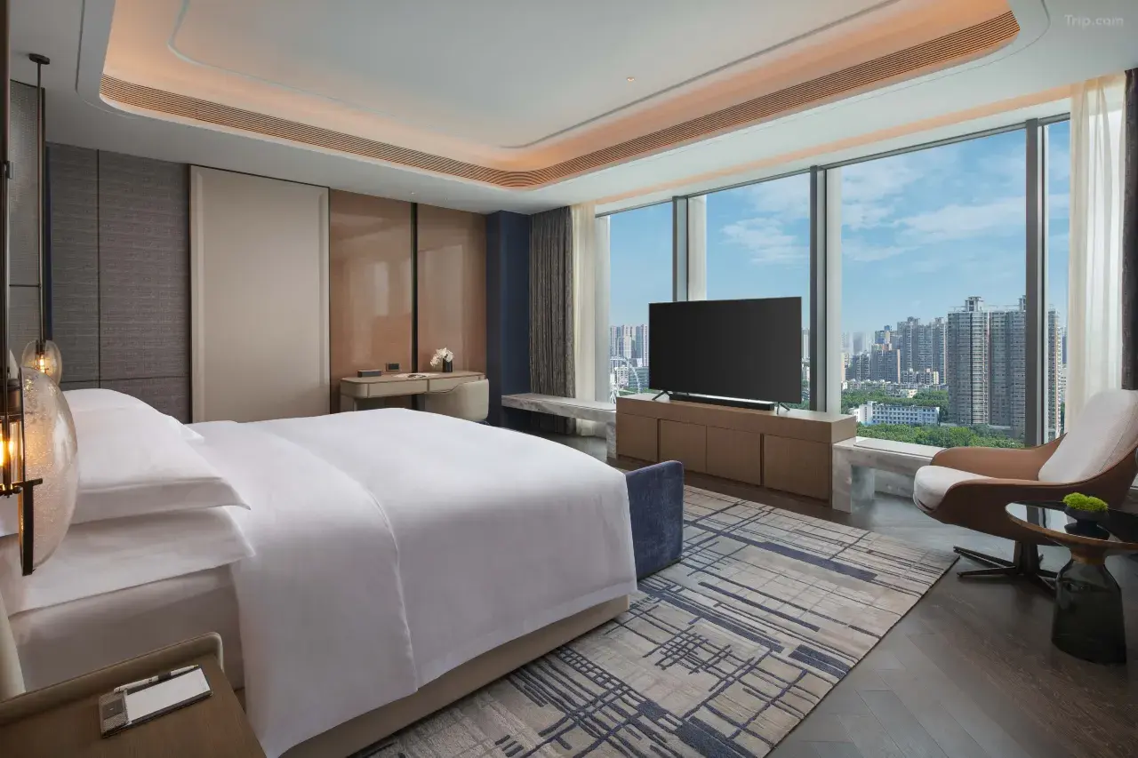 Modern luxury hotel bedroom with floor-to-ceiling windows and city views.