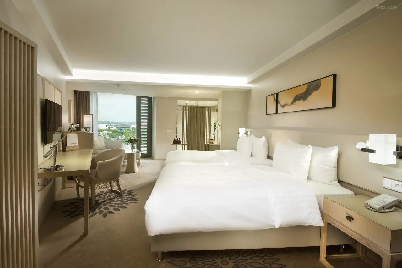 Modern hotel room with two white beds, a desk, and large window.