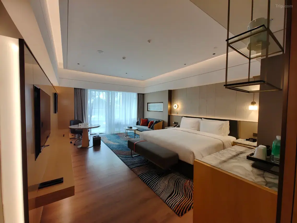 Spacious hotel room with a large bed, sofa, desk, and a bright window.