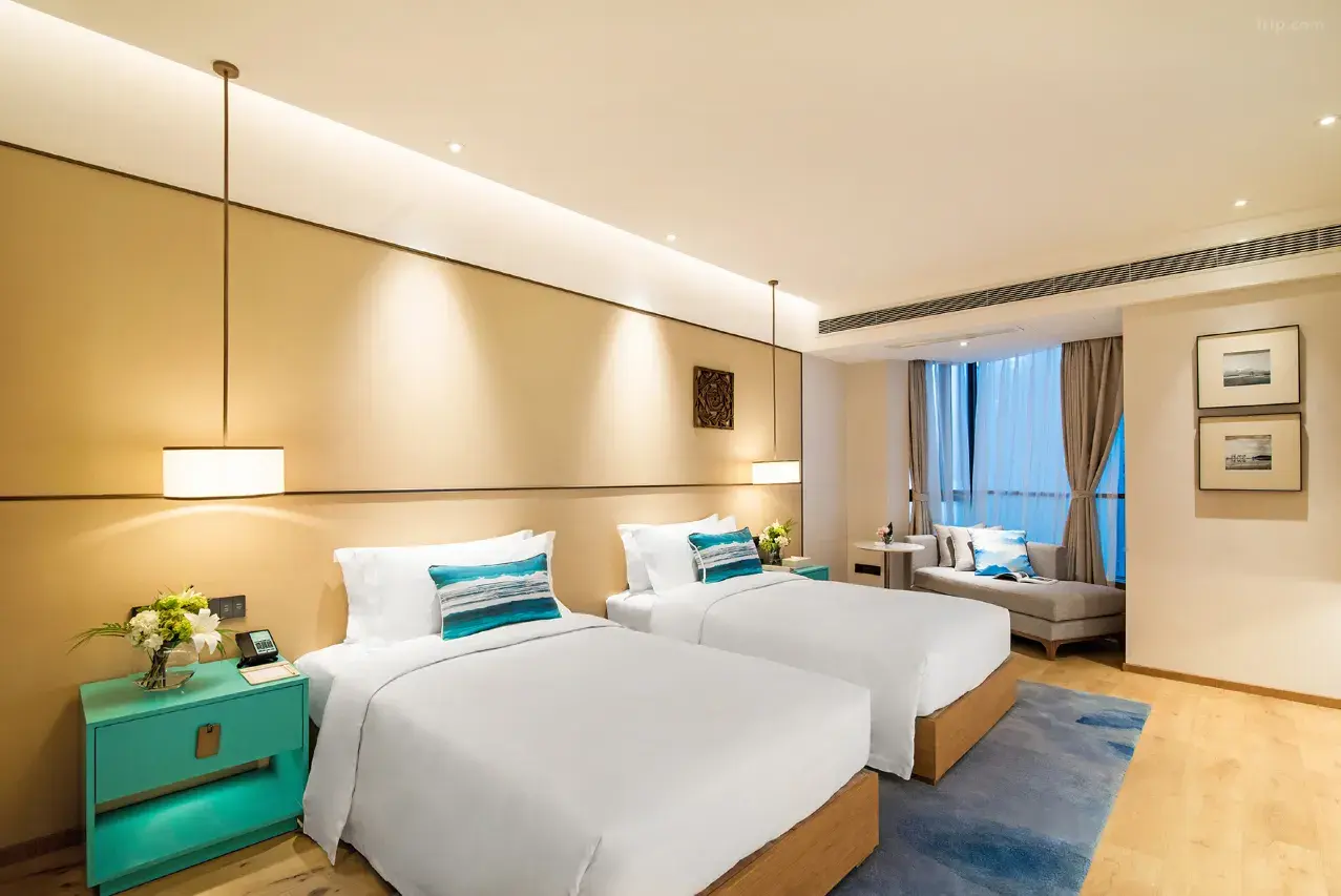 Modern hotel room with two beds, blue accents, and a window lounge area.