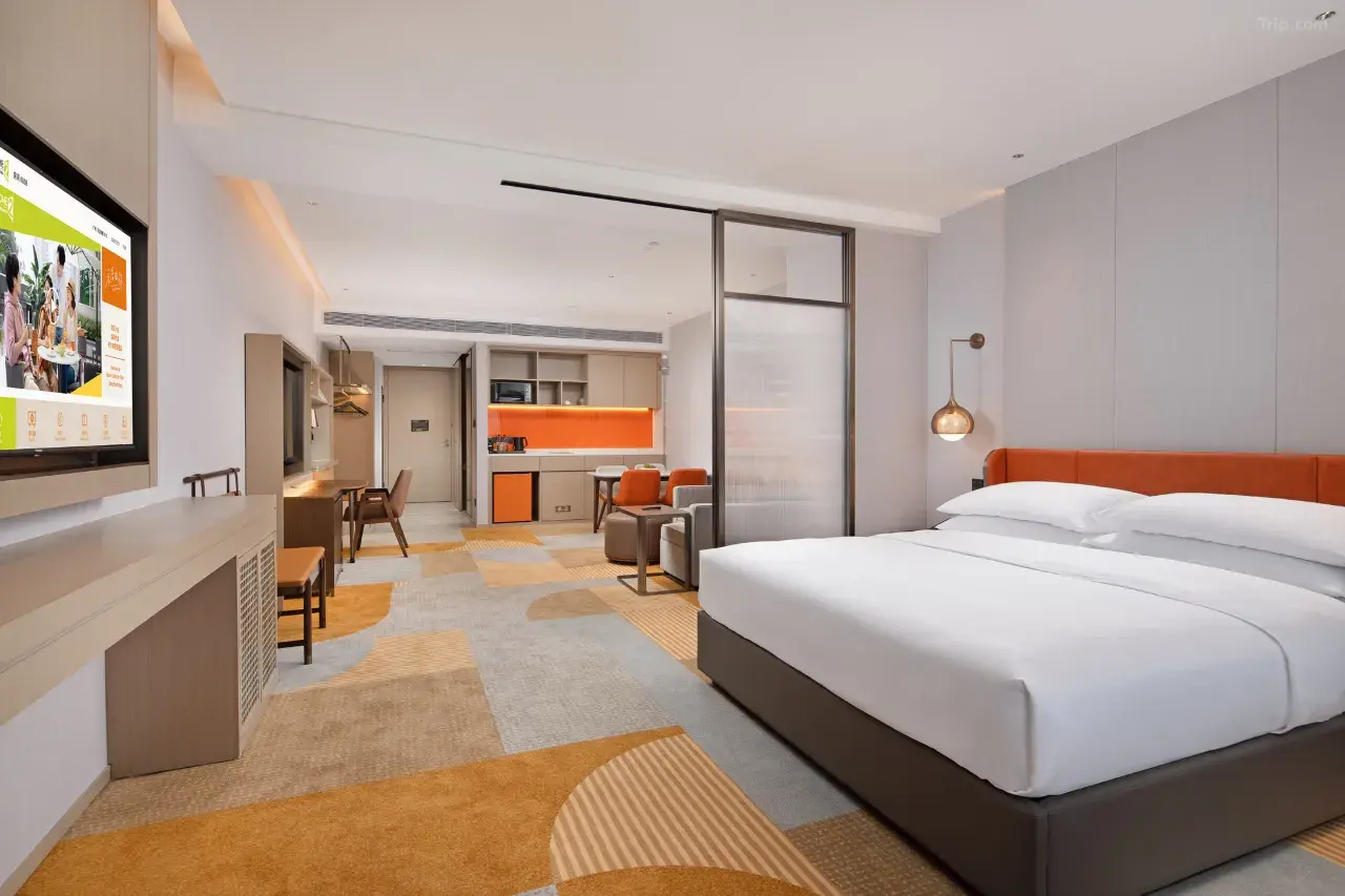Modern hotel suite with a king bed, living area, and kitchenette.