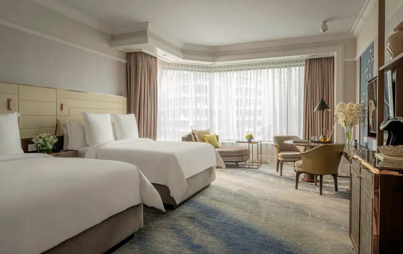 Modern hotel room with two queen beds, a seating area, and large windows.