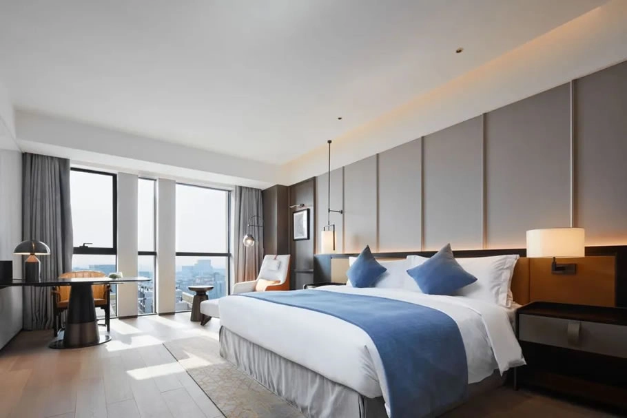 Hotel room with large windows, desk, and king-sized bed with blue accents.