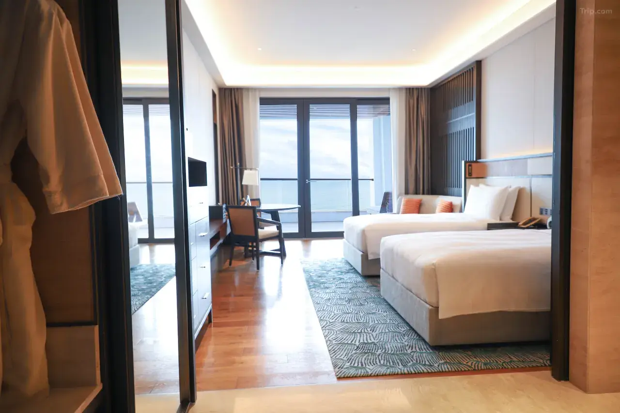 Hotel room interior with two beds, desk, balcony overlooking the ocean, and a robe hanging in the foreground.