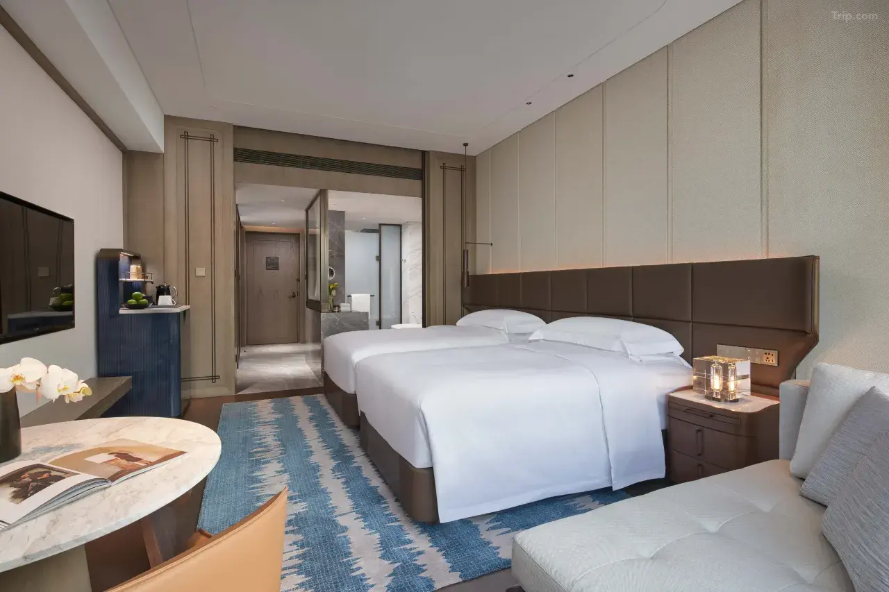 Modern hotel twin room with white bedding, blue rug, and marble table.