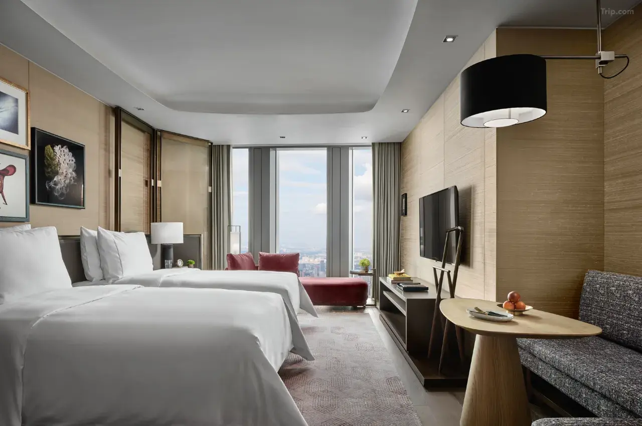 Modern hotel room with two twin beds, city view, and sitting area.