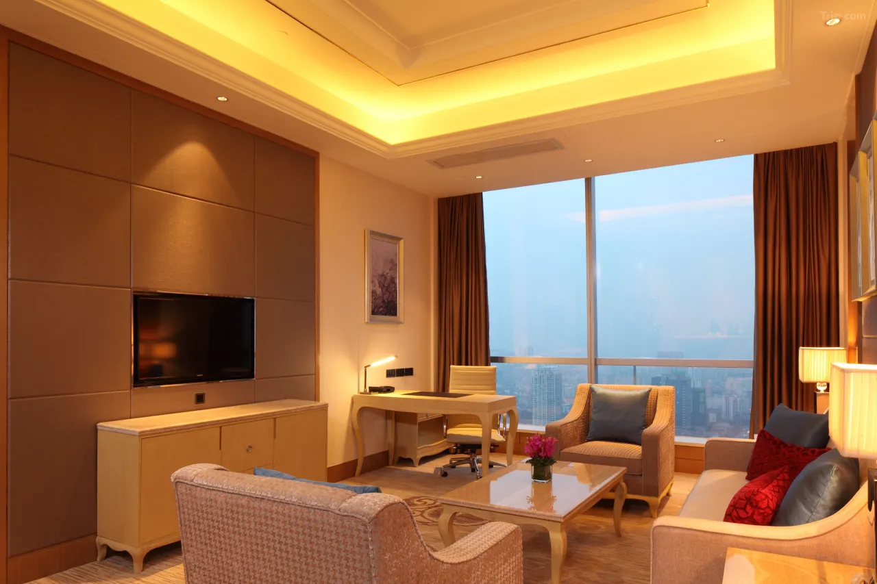 Spacious hotel living room with seating area, desk, TV, and city view from large windows.