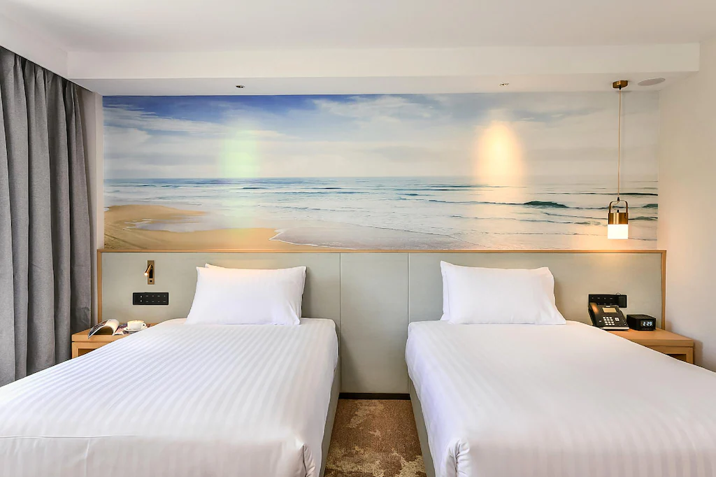 Two single beds in a hotel room with a beach mural above the headboards.